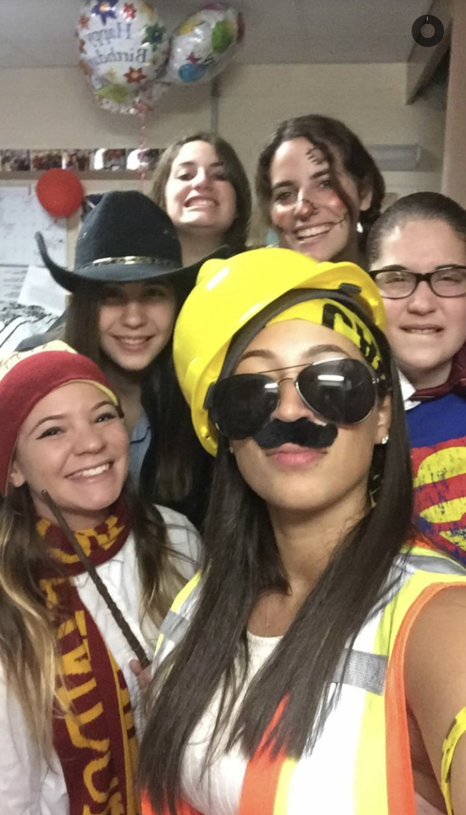 Friends in costume crowded into a dorm room decorated with birthday balloons